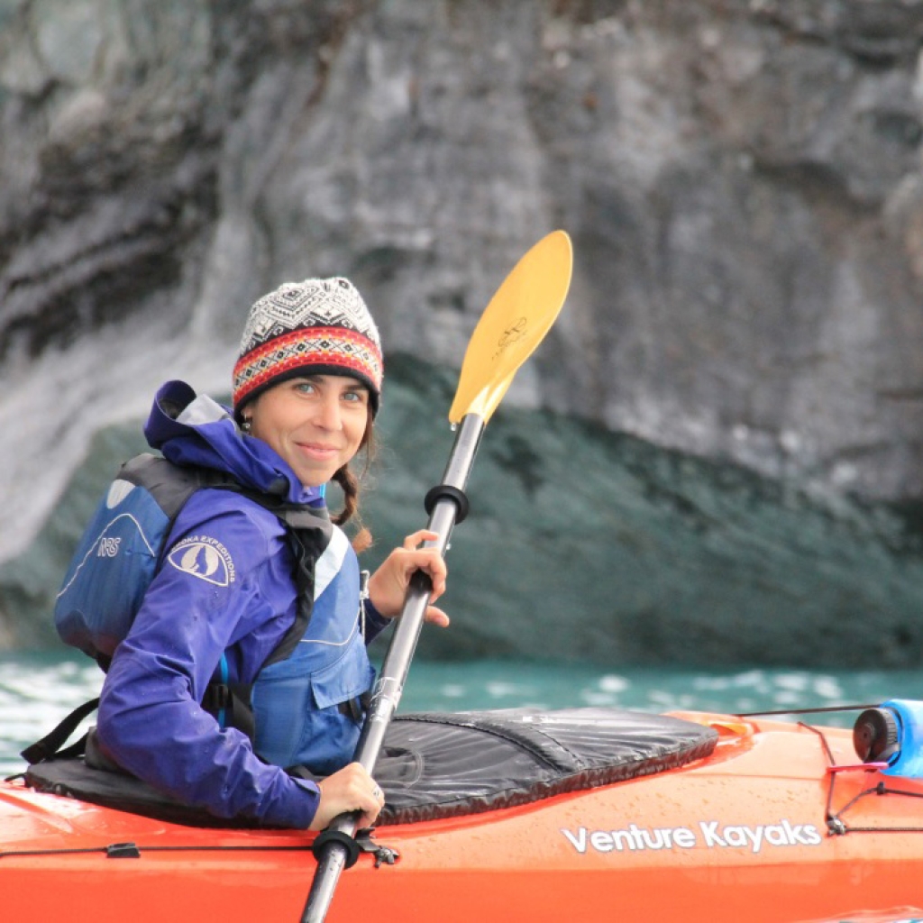 Leah Lamdin smiling at the camera while paddling a sea kayak.