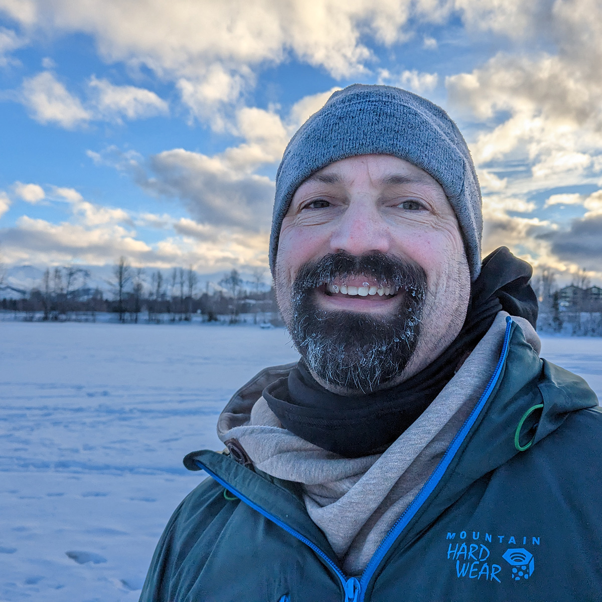 Matt Muir smiling at the camera in a snow-covered field with mountains in the background.